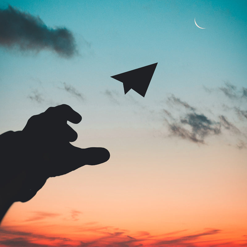 Hand throwing paper-plane in moon's direction.